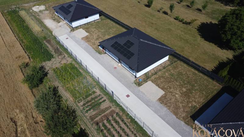 A family house in Podlužany with photovoltaic panels, a garden, and surrounding fields.