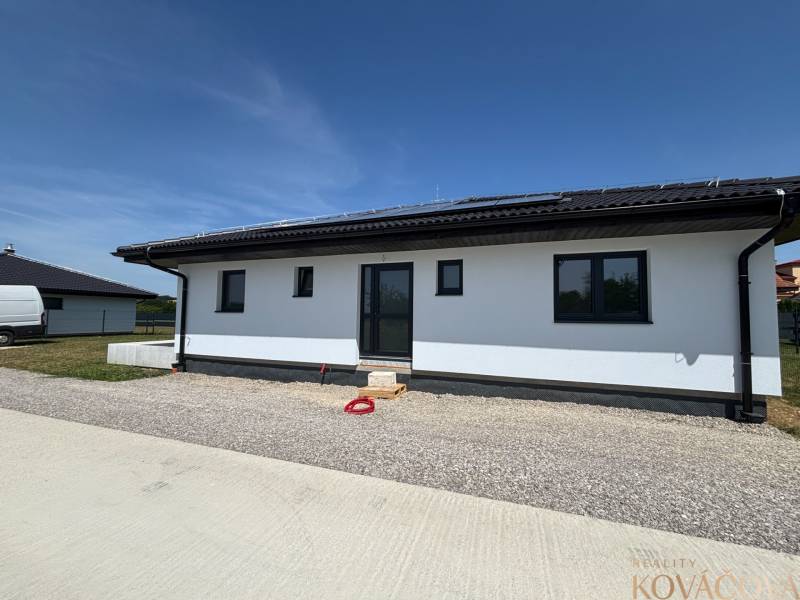 A family house in Podlužany with solar panels and a sloped roof on a gravel plot.