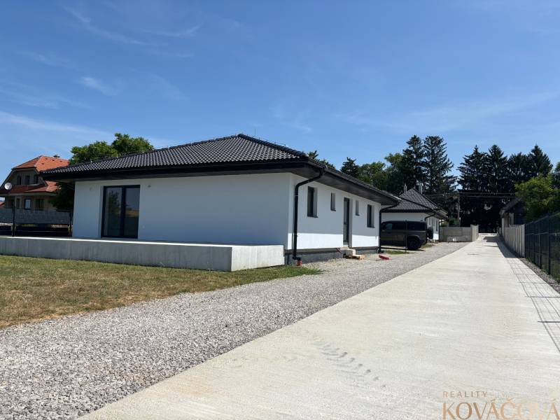 A family house in Podlužany with a white facade, a sloped roof, and a large driveway.