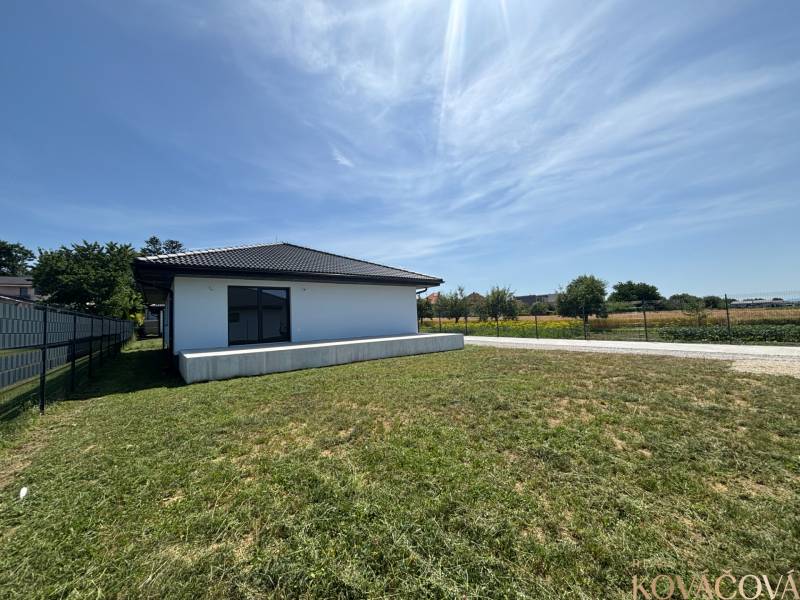 A family house in Podlužany with a large lawn, next to a dirt road and a fence.