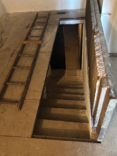 Hidden stairs leading to an underground space, next to an old wooden ladder, close to recreational grounds.