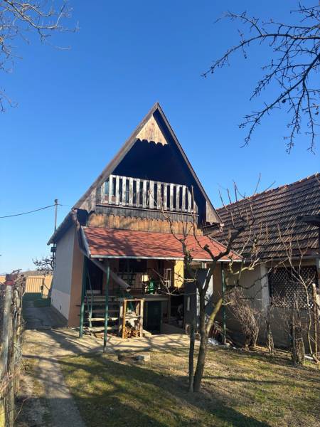 A cottage with a sloped roof and a veranda, surrounded by garden recreational grounds.