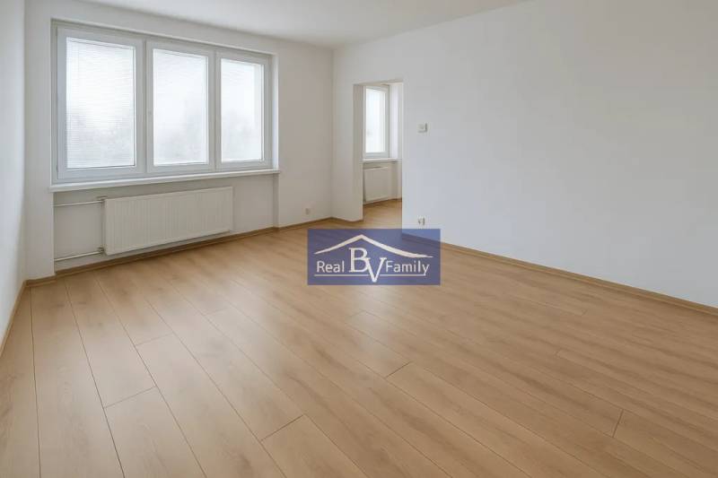 A spacious room with wooden flooring and large windows in a 2-room apartment.