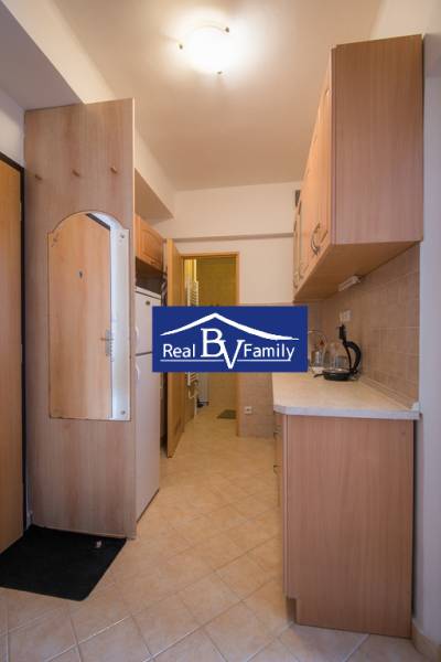Kitchen corner in a studio apartment with a wooden kitchen unit and ceramic floors.