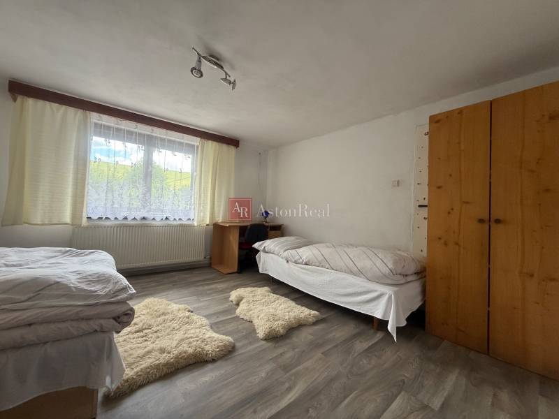 A room with two beds, a wooden wardrobe, a table, and carpets in a family house.
