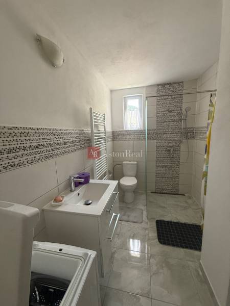A bathroom in a family house with a shower, toilet, and washing machine, light tiles.