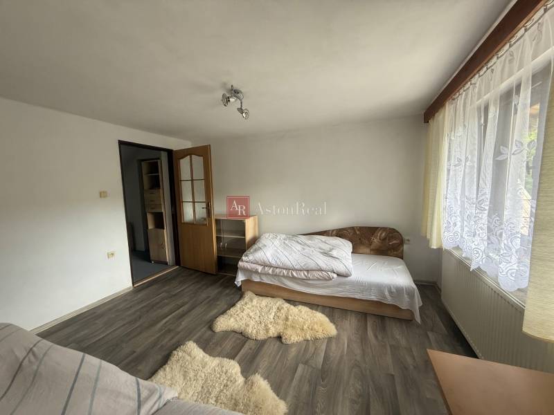 A room with a bed, wooden floor, and a window with a white curtain in a family house.