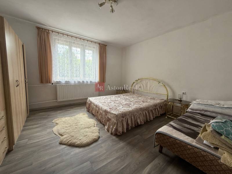 A bedroom in a family house with a bed and a wardrobe, light curtains on the window.