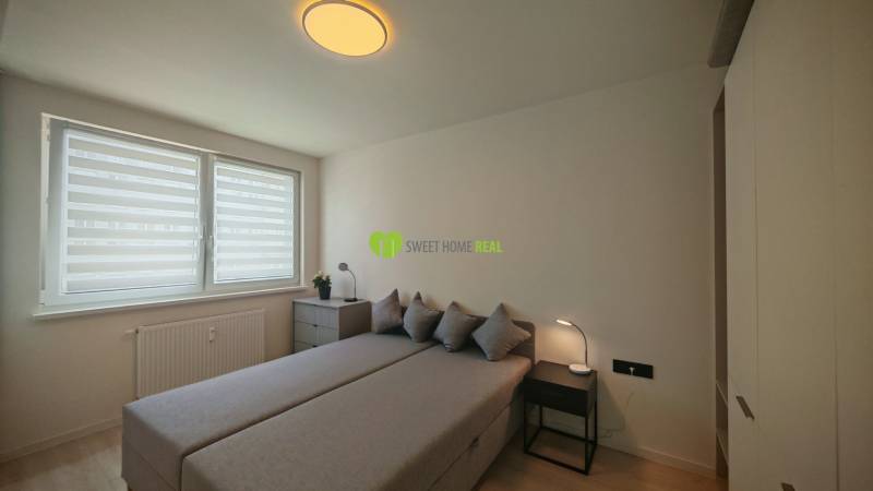 A bedroom with a bed, a cabinet, and windows in a studio apartment, neutral colors.