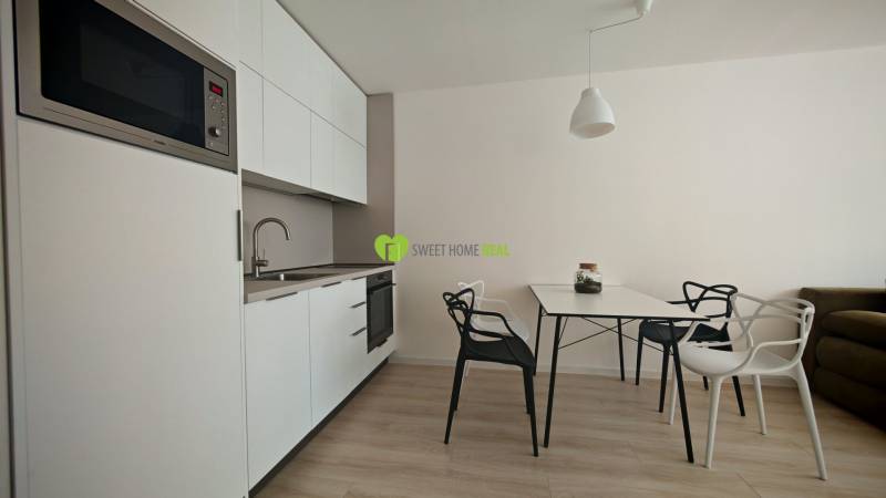 Kitchen corner in a studio apartment, white cabinets, table with chairs, wooden floor.
