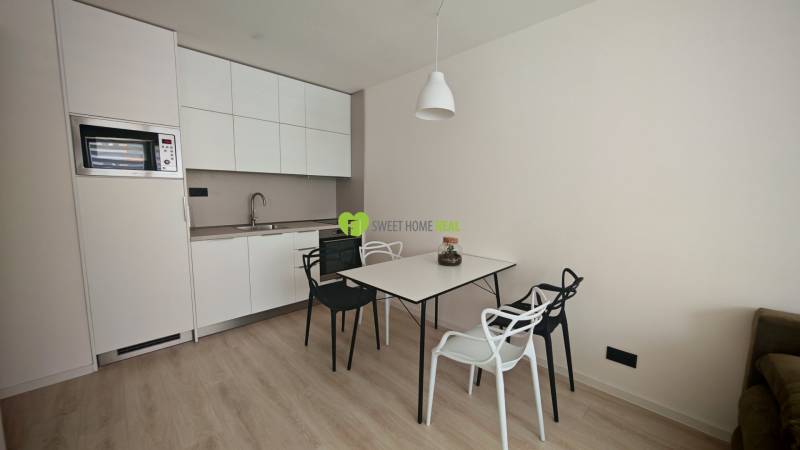 Kitchen in a studio apartment with a dining table and chairs, light wooden floors.