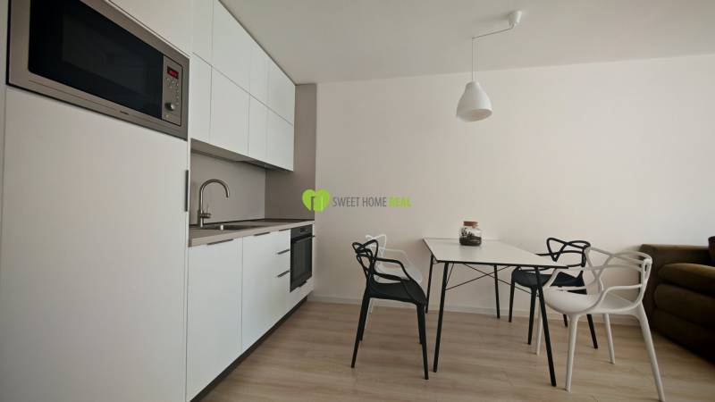 Kitchen corner in a studio apartment with white cabinets and a dining table.