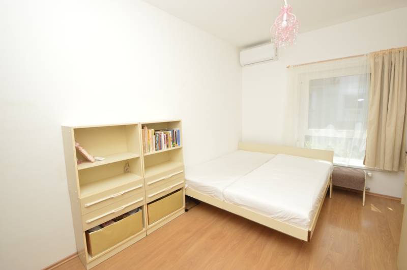 Bright bedroom in a 2-room apartment with a bed, bookshelf, and air conditioning.