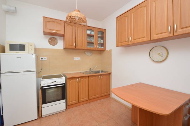A kitchen in a 2-room apartment with wooden furniture, appliances, and ceramic tiles.