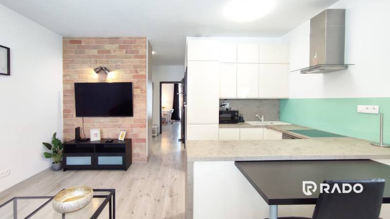 Living room with a kitchenette in a 2-room apartment, brick, TV, wooden floor.