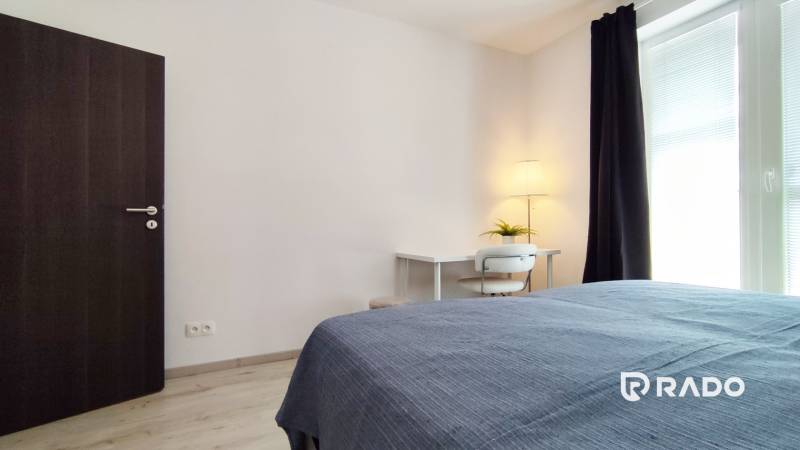 Bedroom in a 2-room apartment with a desk, lamp, and bed.