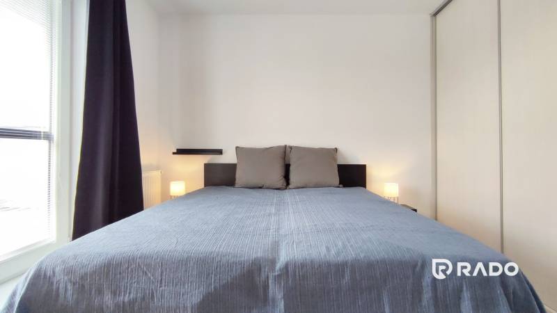 Bedroom in a 2-room apartment with a large bed, window with dark curtains.