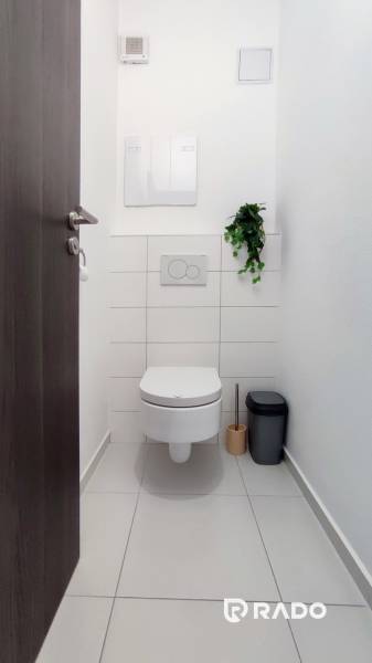 Toilet in a 2-room apartment with white tiles and cleaning supplies.
