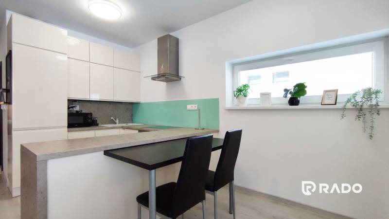 A kitchen in a 2-room apartment with a bar counter, stools, and decorative plants on the windowsill.