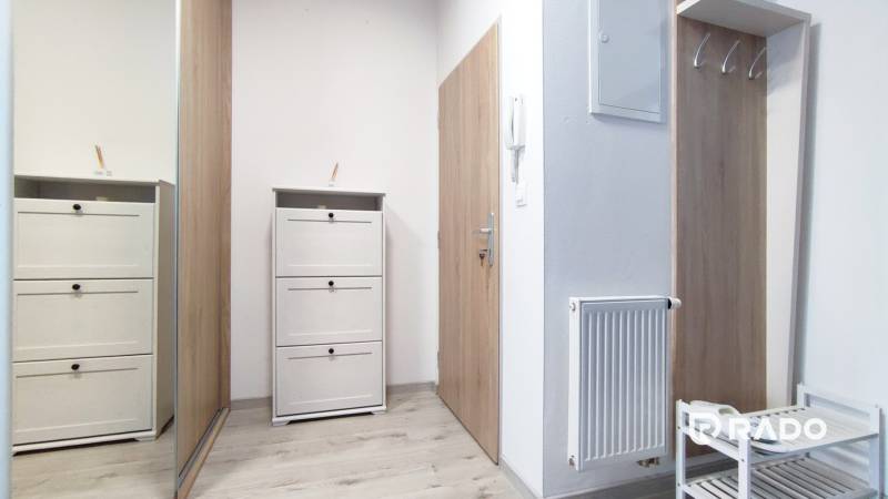 A hallway with white furniture and coat hooks in a 2-room apartment, light wooden floors.