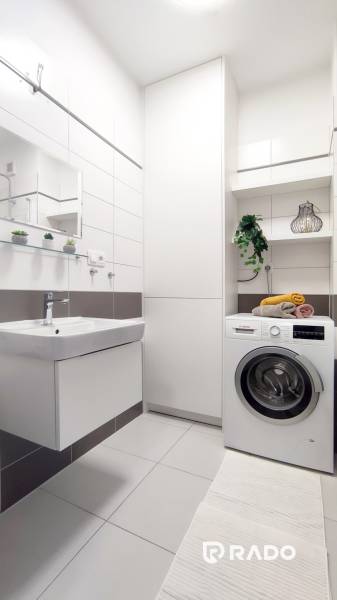Bathroom in a 2-room apartment with a washing machine, sink, and shelves with decorations.