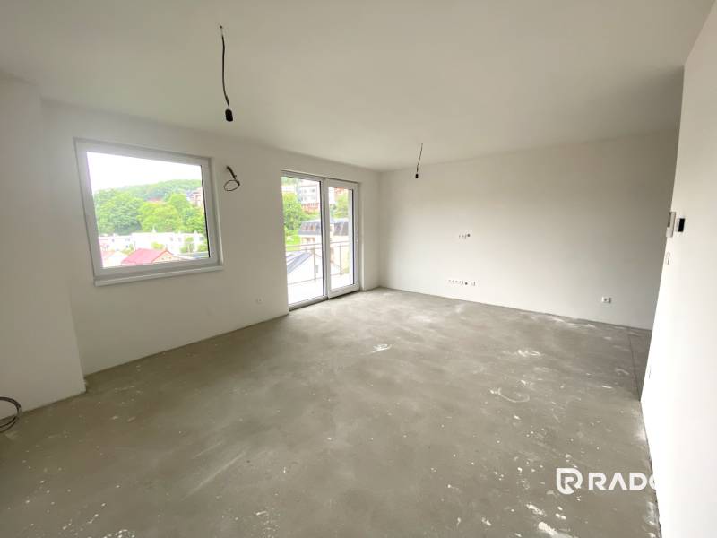 A spacious room of a 2-room apartment with large windows and a concrete floor.