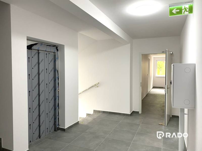 A corridor with a staircase, an elevator, and open doors to a 2-room apartment.