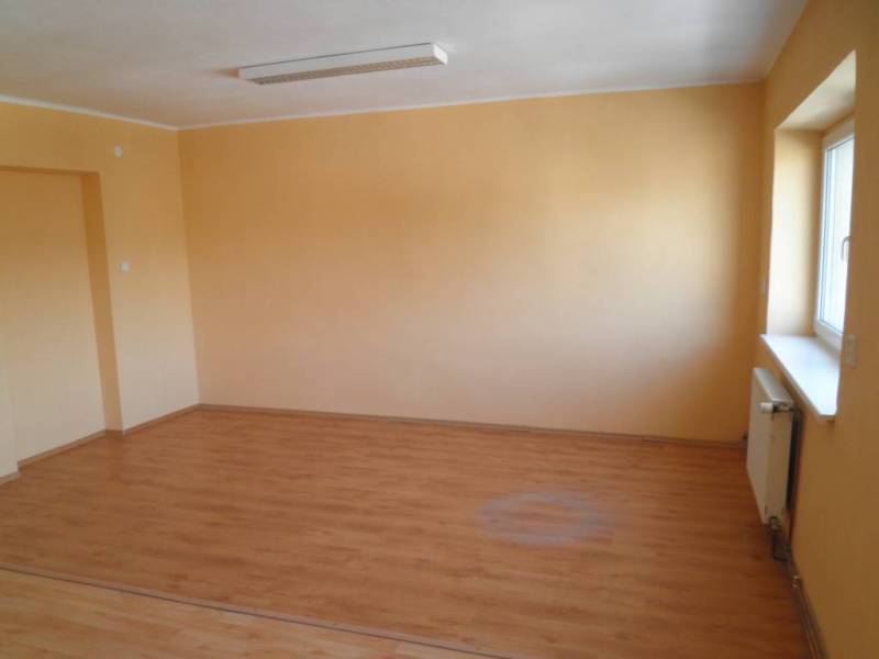 An empty office with wooden flooring and yellow walls, illuminated by daylight.