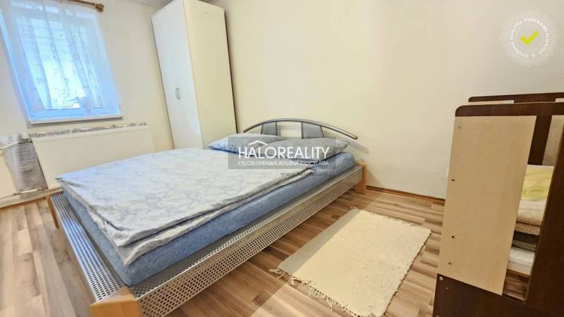 A bedroom in a family house, simply furnished with a bed, a cabinet, and a wooden floor.