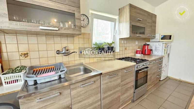 A kitchen in a family house with appliances, wooden cabinets, and a window with plants.