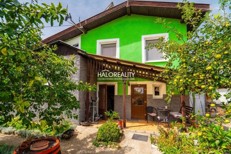 A family house in Banská Štiavnica with a wooden veranda, surrounded by greenery and fruit trees.