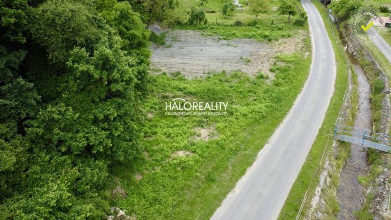 Residential plots in Selce by the road, bordered by greenery and a stream.