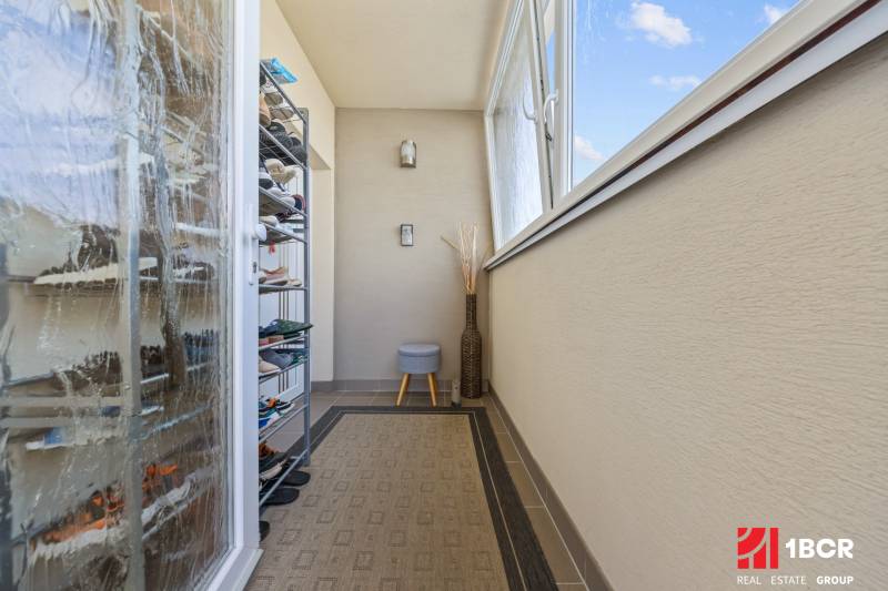 Balcony in a 4-room apartment with a shoe cabinet, carpet, glazing, open window.