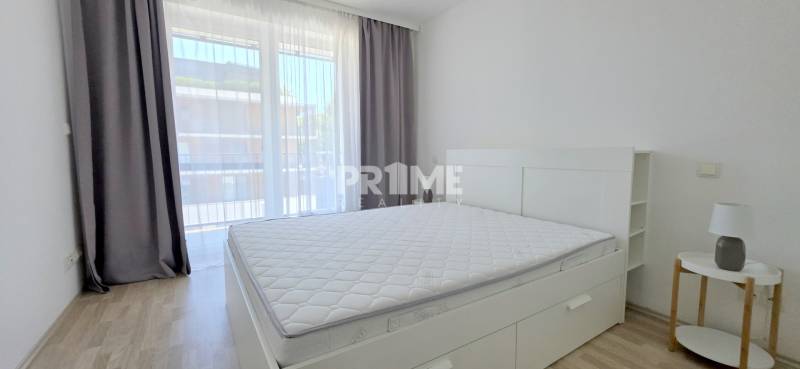 Bright bedroom with a large window, bed, and nightstand in a 2-room apartment.