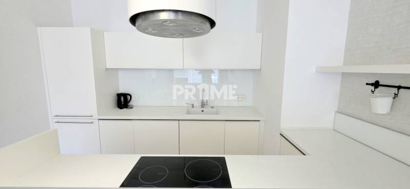 White kitchen with a cooktop and range hood in a 2-room apartment.