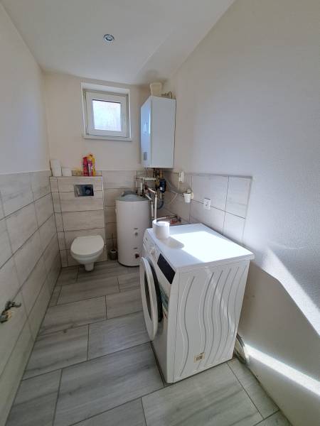 Laundry room in a family house with a washing machine, boiler, and toilet.