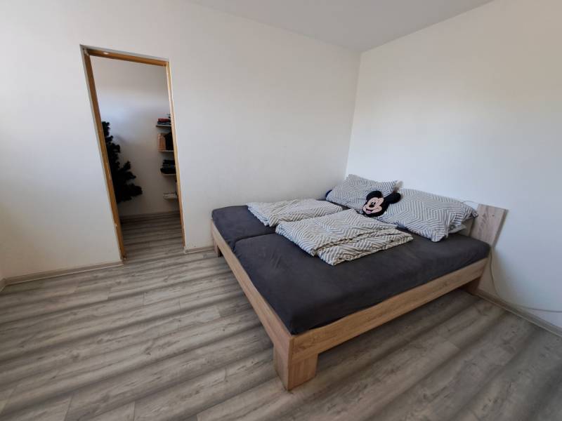 A bedroom in a family house with a bed, burgundy floor, and an entrance to the pantry.