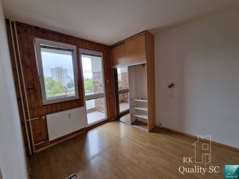 An empty room in a 4-room apartment with wooden panels and a view of the balcony.