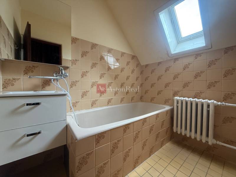 A bathroom in a family house with a bathtub, radiator, and skylight.