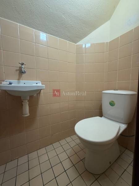 A toilet with a sink in a family house, tiled with beige tiles.