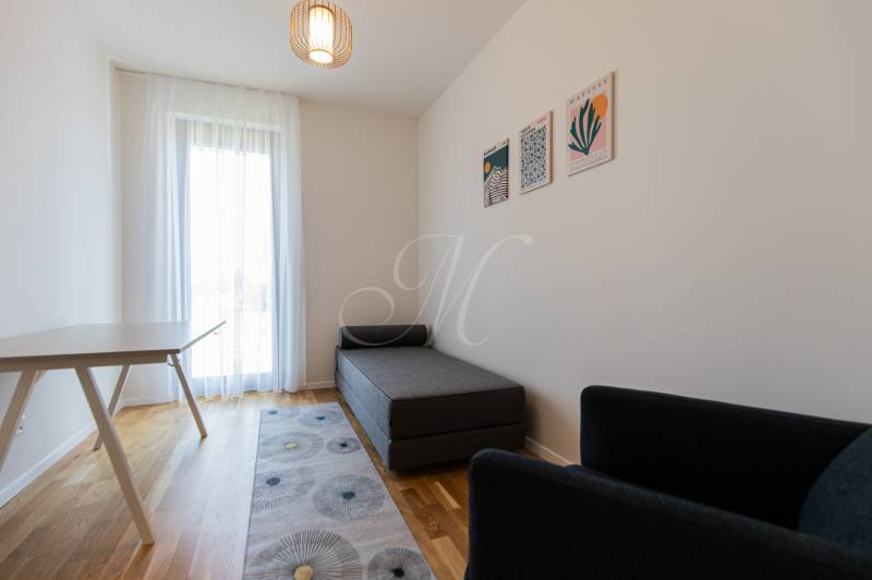 A room in a 3-room apartment with a lounger, a table, a chair, and wall decoration.
