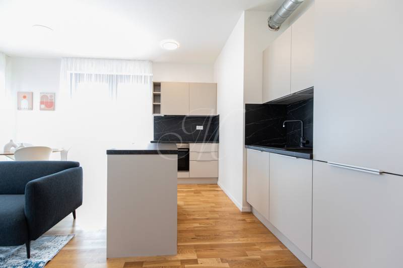 A kitchen in a 3-room apartment with gray furniture, wooden flooring, and a dining table.
