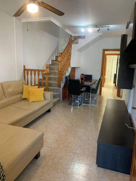 Living room of a family house with a beige sofa, dining table, and wooden staircase.