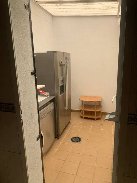 Laundry room in a family house with a refrigerator, washing machine, and a small table on a tiled floor.