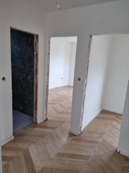 A hallway in a 4-room apartment with a wooden floor and open doors.