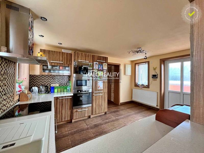 A kitchen in a family house with wooden furniture, built-in appliances, and a large window.