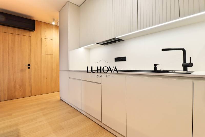 A kitchen in a 2-room apartment with wooden flooring and white cabinets.