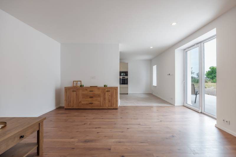 Interior of a family house with wooden flooring, a cabinet, and sliding doors to the terrace.
