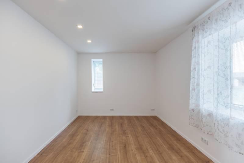 A room in a family house, white walls, wooden floor, a sash window with a light curtain.