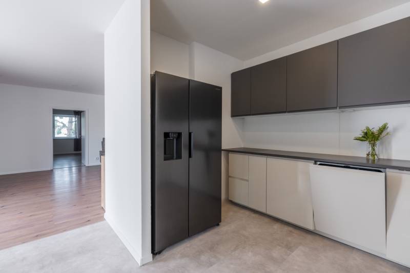 A modern kitchen in a family house with a black refrigerator and light cabinets.